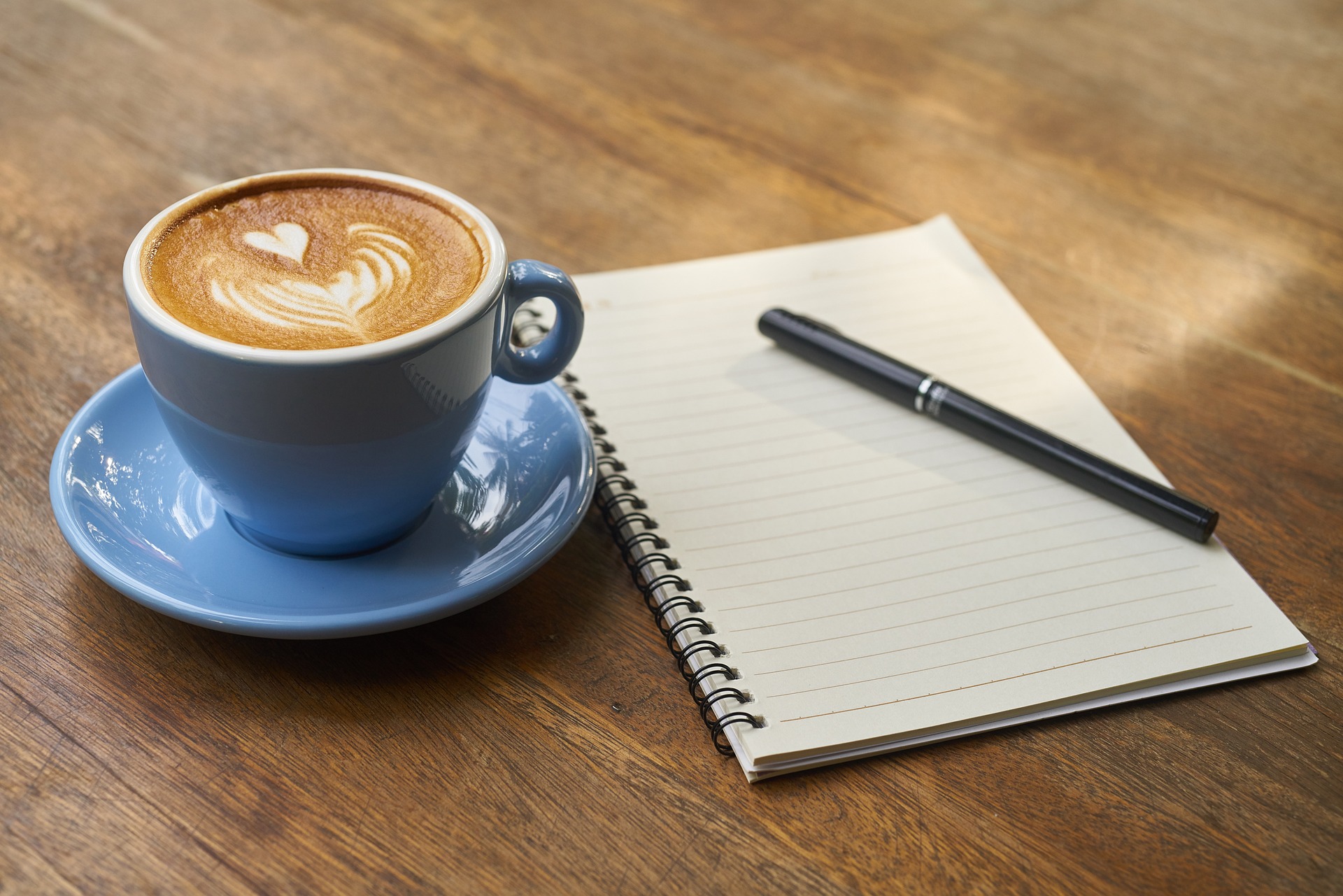 A cup of coffee resting next to a notebook on top of a table