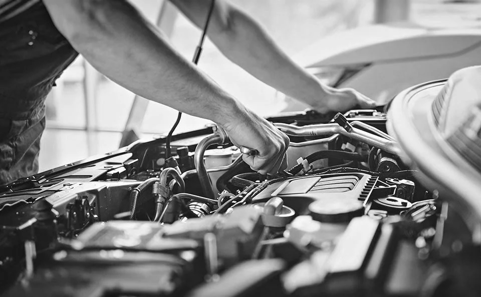 A grayscale image of a man working inside the hood of a vehicle